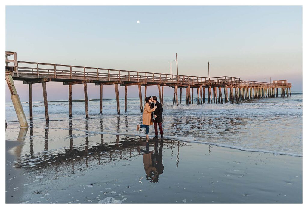 couple standing in front of pier with moon in sky Avalon Beach Engagement Session