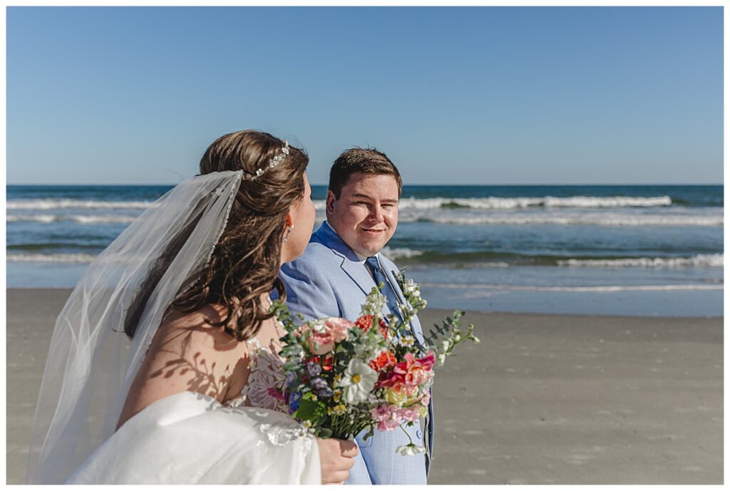 "Lauren and Zach exchanging vows on the beach, surrounded by family and rose petals."