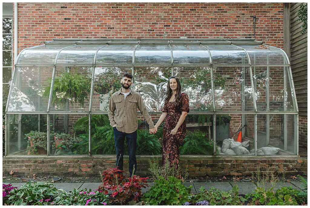 engaged couple standing in front of a green house