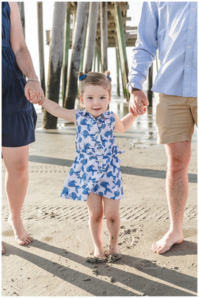 A little girl holding hands with her parents on beach in Ocean City NJ