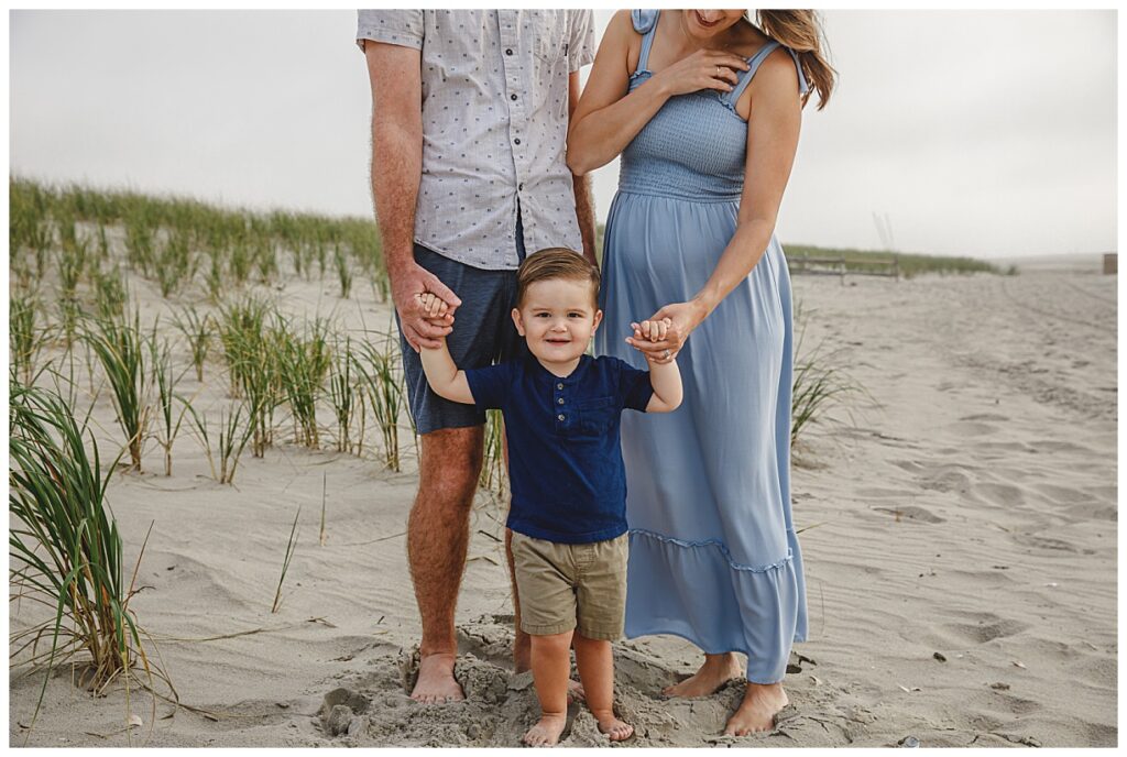 A cute little boy standing with his parents on beach in Ocean City Nj