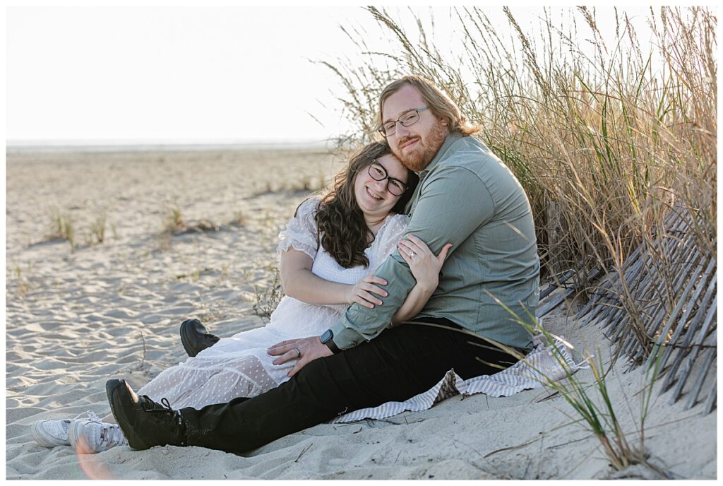 Engaged couple sitting on beach in Cape May NJ
