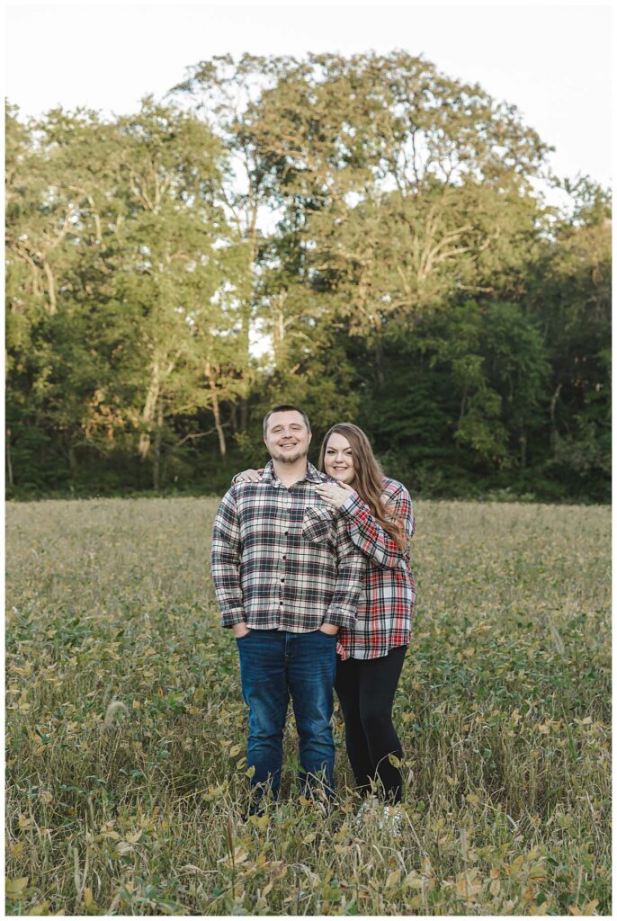 enaged couple standing in field posing for photos