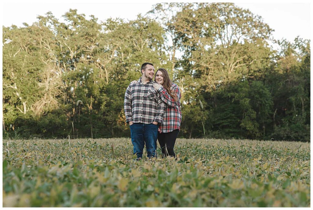 engaged couple standing in a field posing for photos