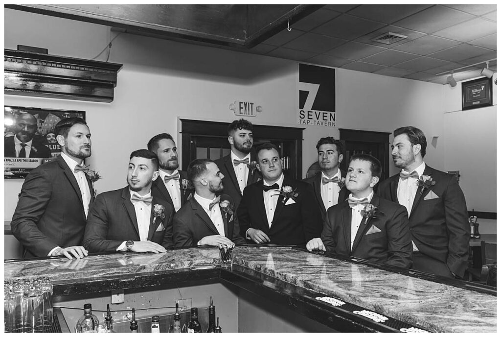 groom and groomsmen sitting at bar looking in different directions