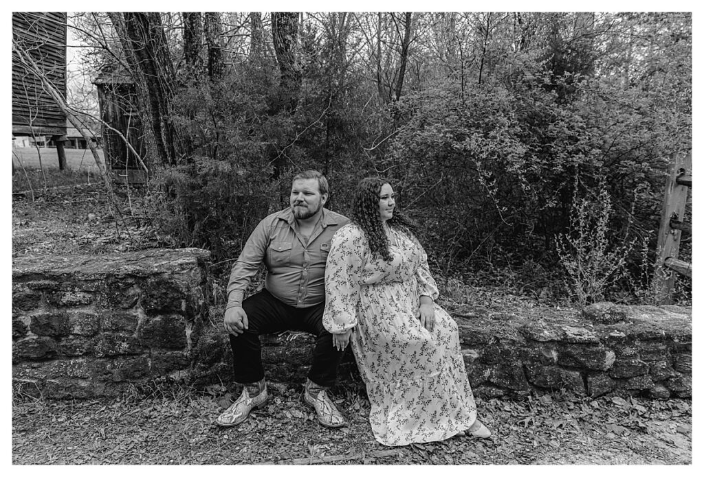 black and while photo of engaged couple sitting on a stone wall