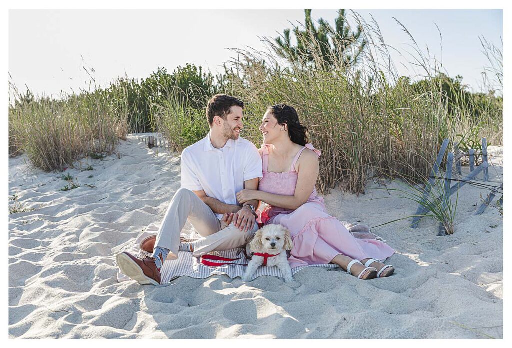 couple sitting on the beach in cape may with their dog for their engagement session